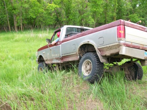 1988 Ford F-150 - A two-tone Ford pickup truck navigates a grassy incline with trees in the background.