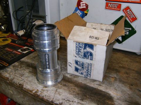 2000 Ford E350 - A machined aluminum part and its original packaging are on a wooden surface.