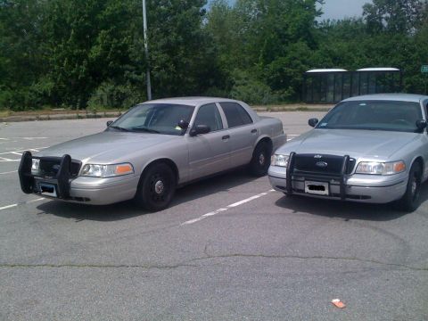 2009 Ford Crown Victoria - Two silver 2009 Ford Crown Victorias, likely police cruisers, are parked side-by-side in a lot.