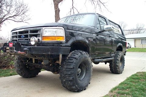 1995 Ford Bronco - Black full-size Ford Bronco lifted on tall mud-terrain tires and black steel wheels, parked on a residential driveway and shot from the fro…