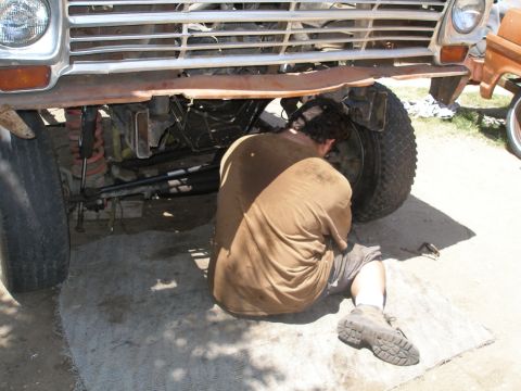 1969 Ford F-250 - A person is working on the front wheel of a truck, with the front grille and bumper visible above.