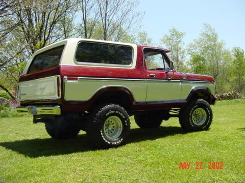 1995 Ford Bronco - A lifted two-tone maroon-and-cream full-size Ford Bronco with a removable hardtop, parked on a green lawn and shot from the rear three-quar…