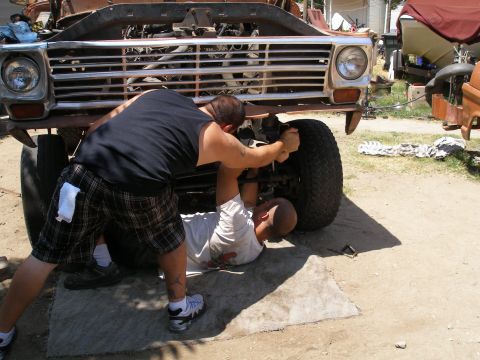 1969 Ford F-250 - Mechanics are working on the front wheel of a truck. The grille suggests a 1967 model year.