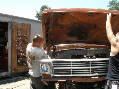 1969 Ford F-250 - Two men work on the engine of an orange truck, its hood propped open. The grille suggests an early 1970s model.
