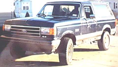 1995 Ford Bronco - Grainy front three-quarter photo of a dark blue late-1980s full-size Ford Bronco with a two-tone lower body, blue oval on the grille, a 4x4…