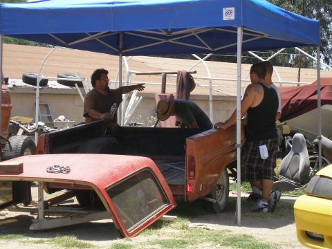 1969 Ford F-250 - A disassembled orange pickup truck and its red cab top are visible under a blue canopy, with several people around.