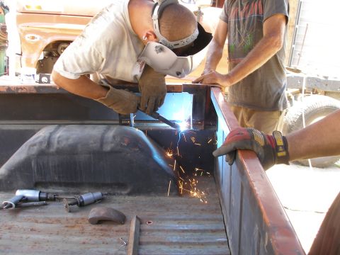 1969 Ford F-250 - Workers weld the frame of a truck bed, with another vehicle partially visible in the background.