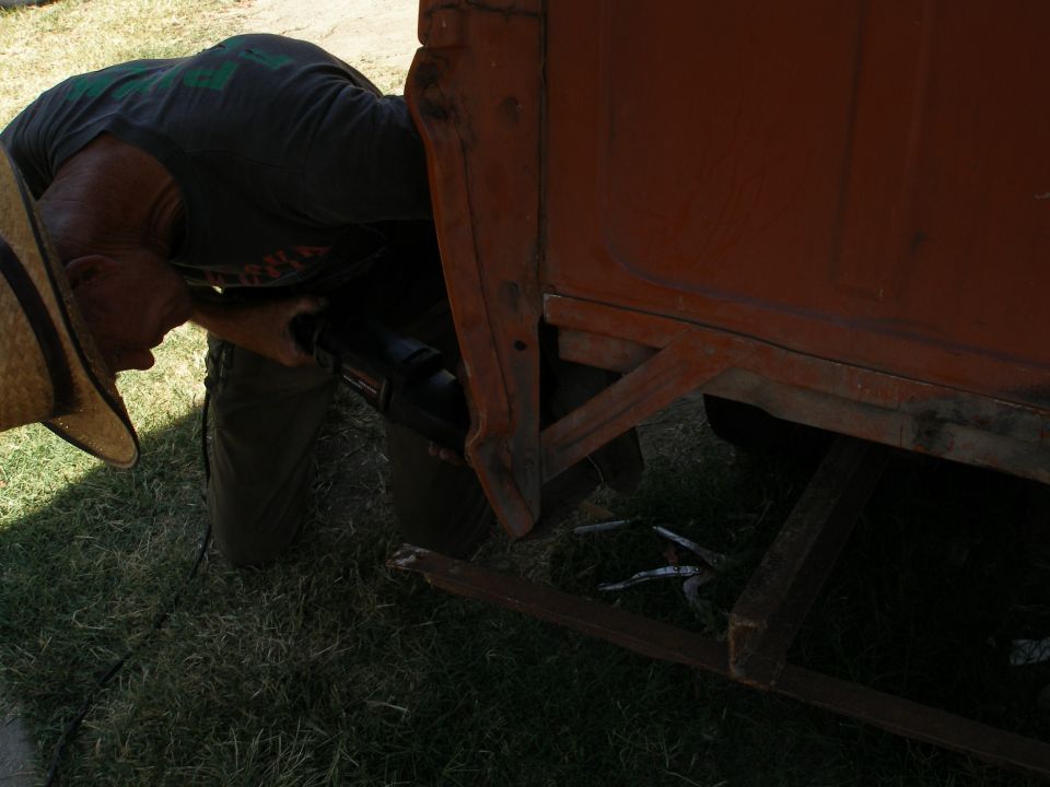 Man in straw hat using a tool on the rusty orange bed of a 1967 Ford F-100 truck
