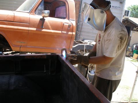 1969 Ford F-250 - A man welds the side of an orange 1967 Ford F-250 truck bed.