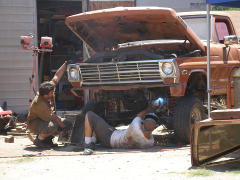 1969 Ford F-250 - Two mechanics work on the front end of an orange truck, with one using a welder to repair the chassis.