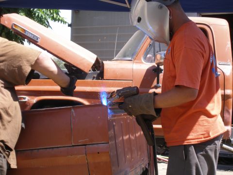 1969 Ford F-250 - Welding a new panel onto the side of an orange pickup truck during repairs.