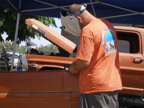 1969 Ford F-250 - A man welds a fender on an orange pickup truck with its hood open.