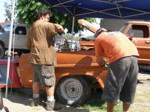 1969 Ford F-250 - Two men work on an orange pickup truck with its hood open, while another truck is visible in the background.