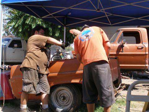 1969 Ford F-250 - Men are working on the side of an orange Ford F-100 pickup truck under a blue canopy.