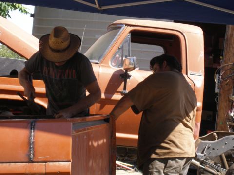 1969 Ford F-250 - Two men are working on the bed of an orange pickup truck, with the hood open. The truck appears to be from the early 1970s.