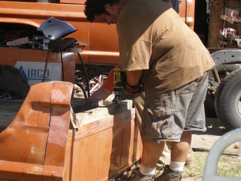 1969 Ford F-250 - Man works on an orange metal part, possibly from a vehicle, with assistance.