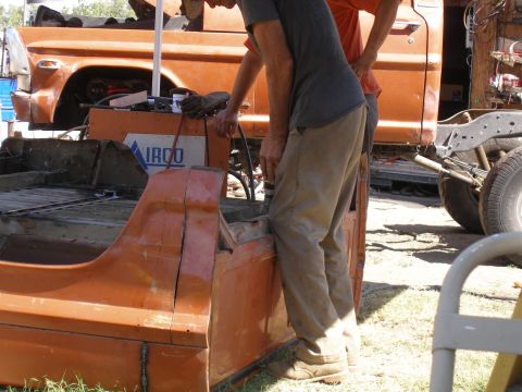 1969 Ford F-250 - Workers are welding or repairing the orange truck bed. Another truck is visible in the background.
