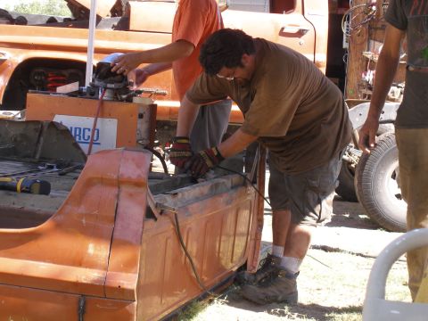 1969 Ford F-250 - Men work on an orange truck bed, possibly a 1967 Ford F-250, with visible damage and repair work.