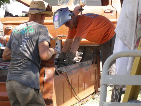 1969 Ford F-250 - Two men are working on the bed of an orange truck, possibly performing repairs or modifications.
