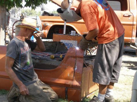 1969 Ford F-250 - Men work on repairing an orange truck bed, with another truck in the background.
