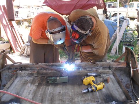 1969 Ford F-250 - Two men are welding on a metal surface, possibly a vehicle frame, with tools scattered around.