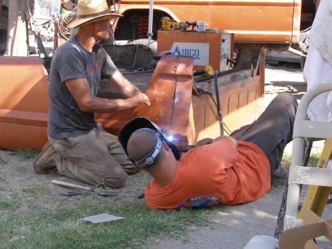 1969 Ford F-250 - Two men work on repairing an orange 1967 Ford F-100 truck bed with welding equipment.