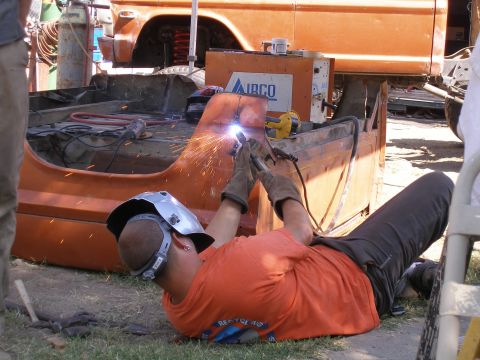 1969 Ford F-250 - A person welds an orange truck bed, with a welding machine and tools nearby. The truck appears to be undergoing repairs or customization.