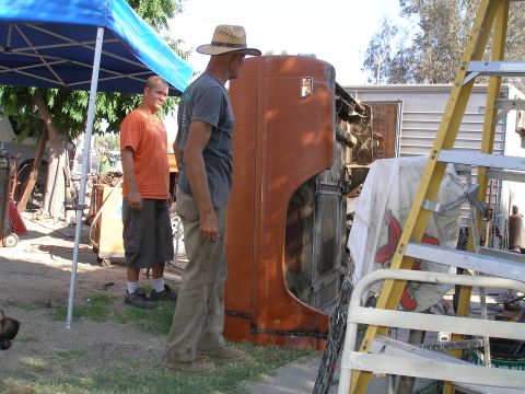 1969 Ford F-250 - A man in a hat looks at an orange truck fender while another man stands nearby under a blue canopy.