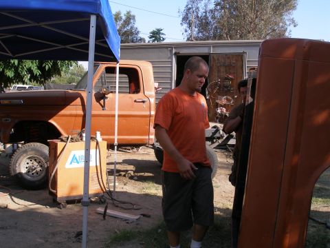 1969 Ford F-250 - A man stands next to an orange pickup truck that appears to be undergoing repairs or modifications.