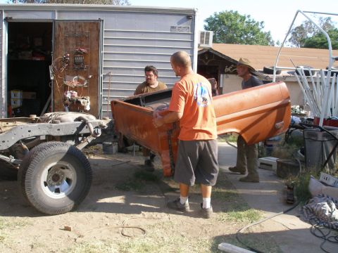 1969 Ford F-250 - Men are seen carrying an orange truck bed next to a bare chassis and a trailer.