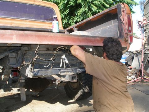 1969 Ford F-250 - A man works on the rear underside of an orange pickup truck, which appears to be a 1973 model based on its body style.