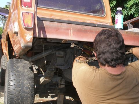1969 Ford F-250 - Man works on the rear axle and wiring of an orange pickup truck. The registry claims it is a 1969 Ford F-250, but the body style does not m…