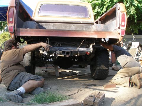 1969 Ford F-250 - Men work on the rear suspension and hitch of a pickup truck, possibly a Ford F-Series from the mid-1970s.