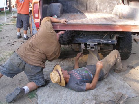 1969 Ford F-250 - Two men are working on the underside of a pickup truck's bed, possibly doing repairs or modifications.