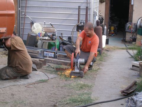 1969 Ford F-250 - A man cuts a Ford F-250 bumper with a chop saw in a yard with another person working on the truck.