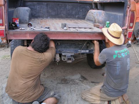 1969 Ford F-250 - Two individuals are seen working on the rear hitch of a pickup truck, with tools and a can of soda nearby.