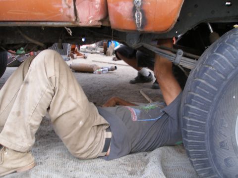 1969 Ford F-250 - A person works on the undercarriage of a truck, with a large tire visible on the right side of the frame.