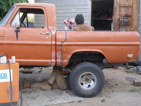 1969 Ford F-250 - A person works on the underside of an orange pickup truck, revealing a welded repair on the bed.
