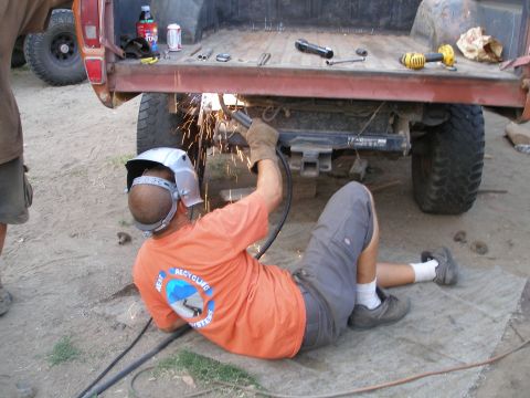 1969 Ford F-250 - A person welds the frame of a red pickup truck bed, with another vehicle partially visible in the background.