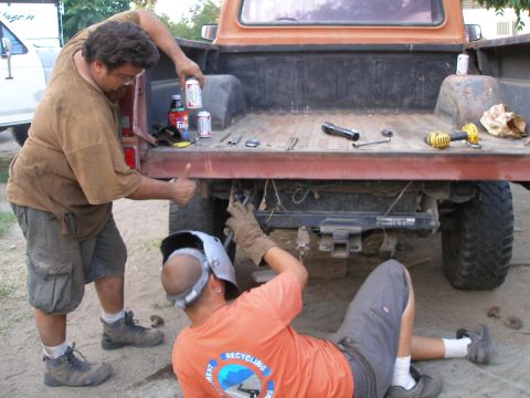 1969 Ford F-250 - Two men are performing maintenance on the rear of a pickup truck, with tools and beverages nearby.