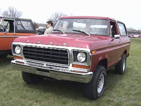 1995 Ford Bronco - A red Ford Bronco is parked on a grassy field next to another vehicle.
