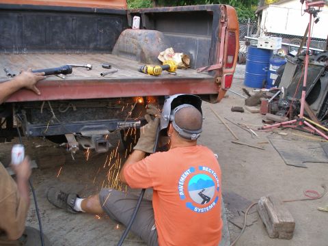 1969 Ford F-250 - Welding sparks fly as a person works on the rear frame of an orange Ford pickup truck.