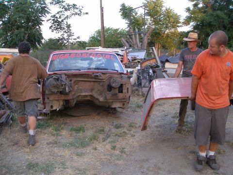 1969 Ford F-250 - Disassembled red pickup truck front end with a banner on the windshield. Two men carry a fender nearby.