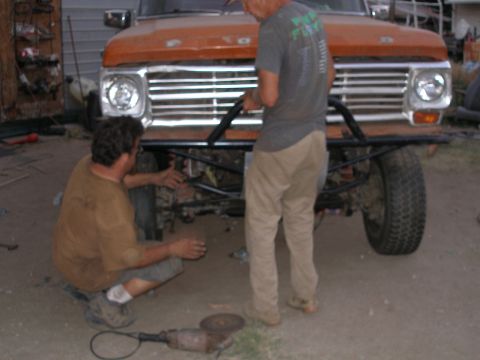 1969 Ford F-250 - Men are working on the front end of an orange Ford F-Series truck, with tools and parts visible.