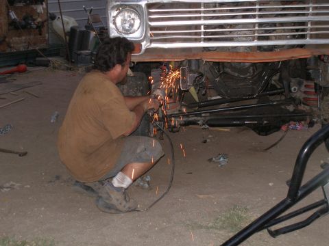 1969 Ford F-250 - A man is using an angle grinder on the front frame of a truck, creating a shower of sparks.