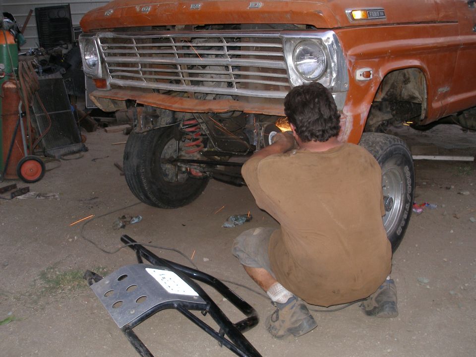 Orange Ford truck front end with a man welding, showing a 1967 grille and headlight