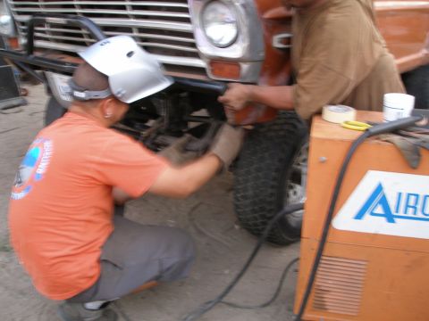 1969 Ford F-250 - Two men work on the front of an orange Ford truck, one welding near the wheel.