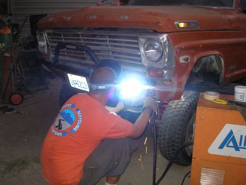 1969 Ford F-250 - A man welds the front fender of a 1969 Ford F-250 pickup truck in a garage setting.