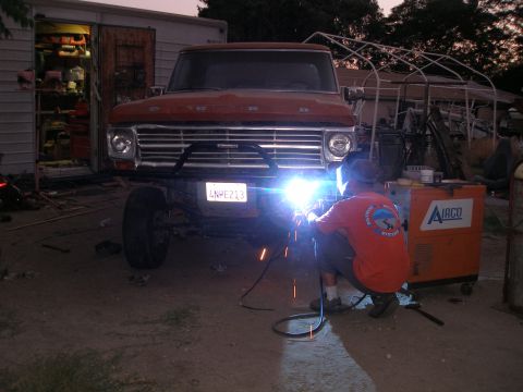 1969 Ford F-250 - Man welding a custom bumper on a 1969 Ford F-250 truck in a garage setting.