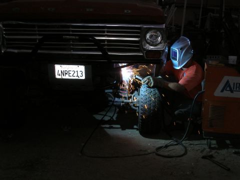 1969 Ford F-250 - A person in a welding mask works on the front of a truck, sparks flying from the bumper area.
